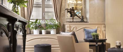 Una habitación con un piano, un sofá, una mesita con plantas y una estatua decorativa.