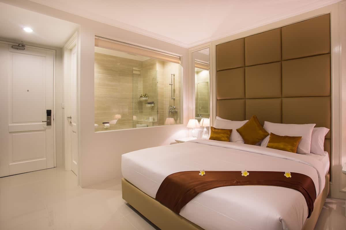A modern hotel room with a large bed, a glass-enclosed shower, and a large mirror.