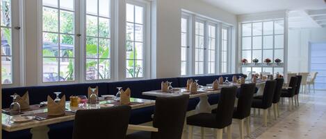A restaurant with long tables, dark blue booths, and white chairs.