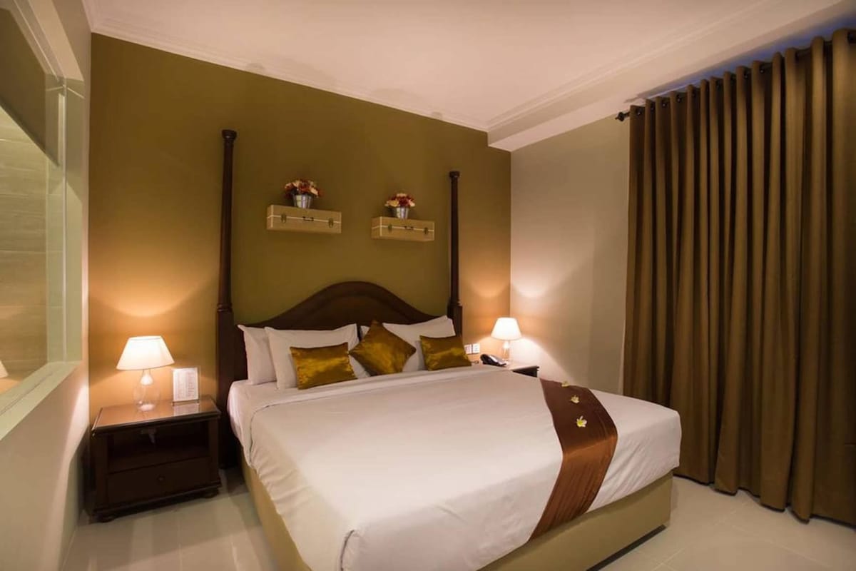 A hotel room with a large bed, two bedside tables with lamps, a wooden headboard, and a window with curtains.