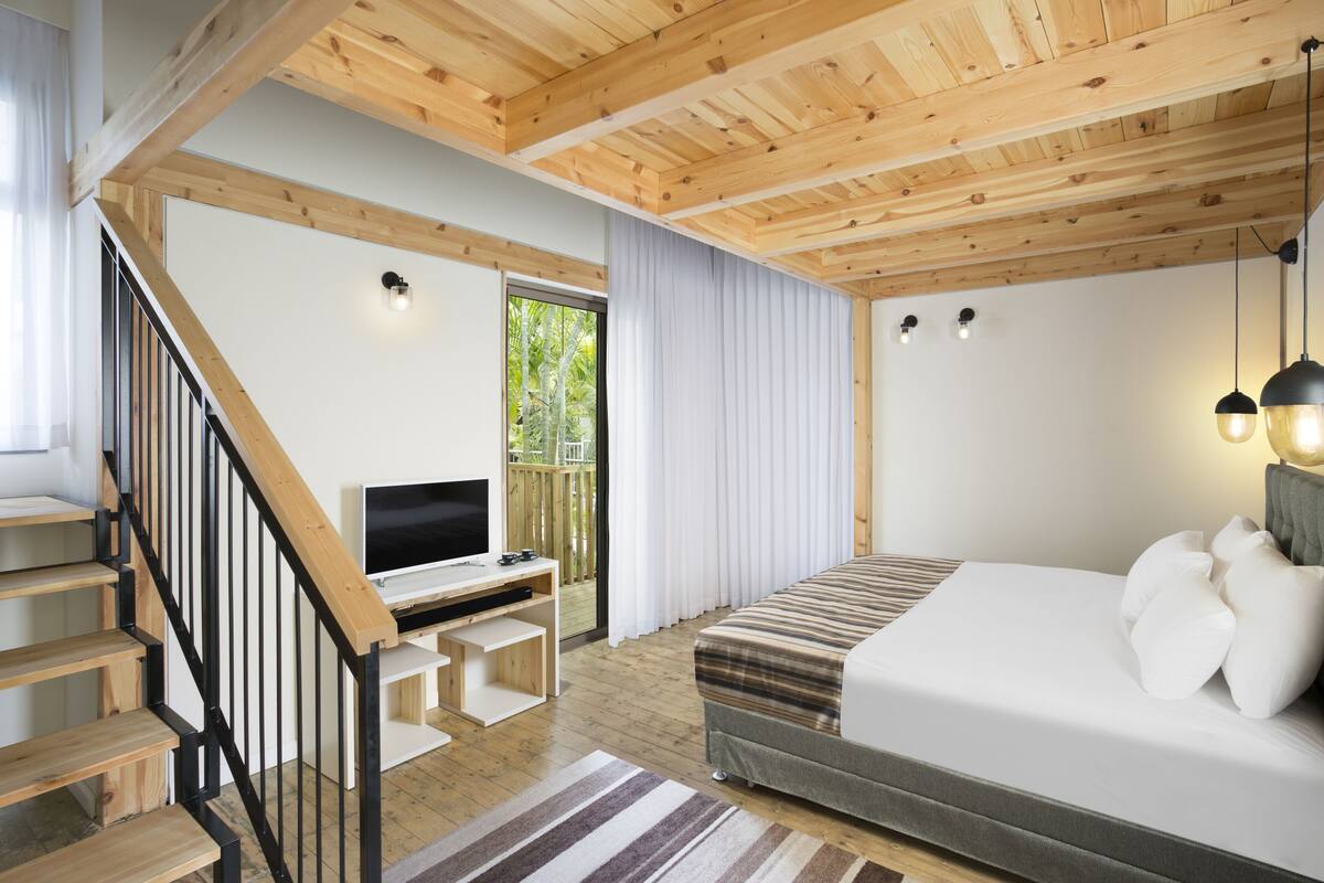 A modern bedroom with a wooden ceiling, a bed, a TV, and a staircase.