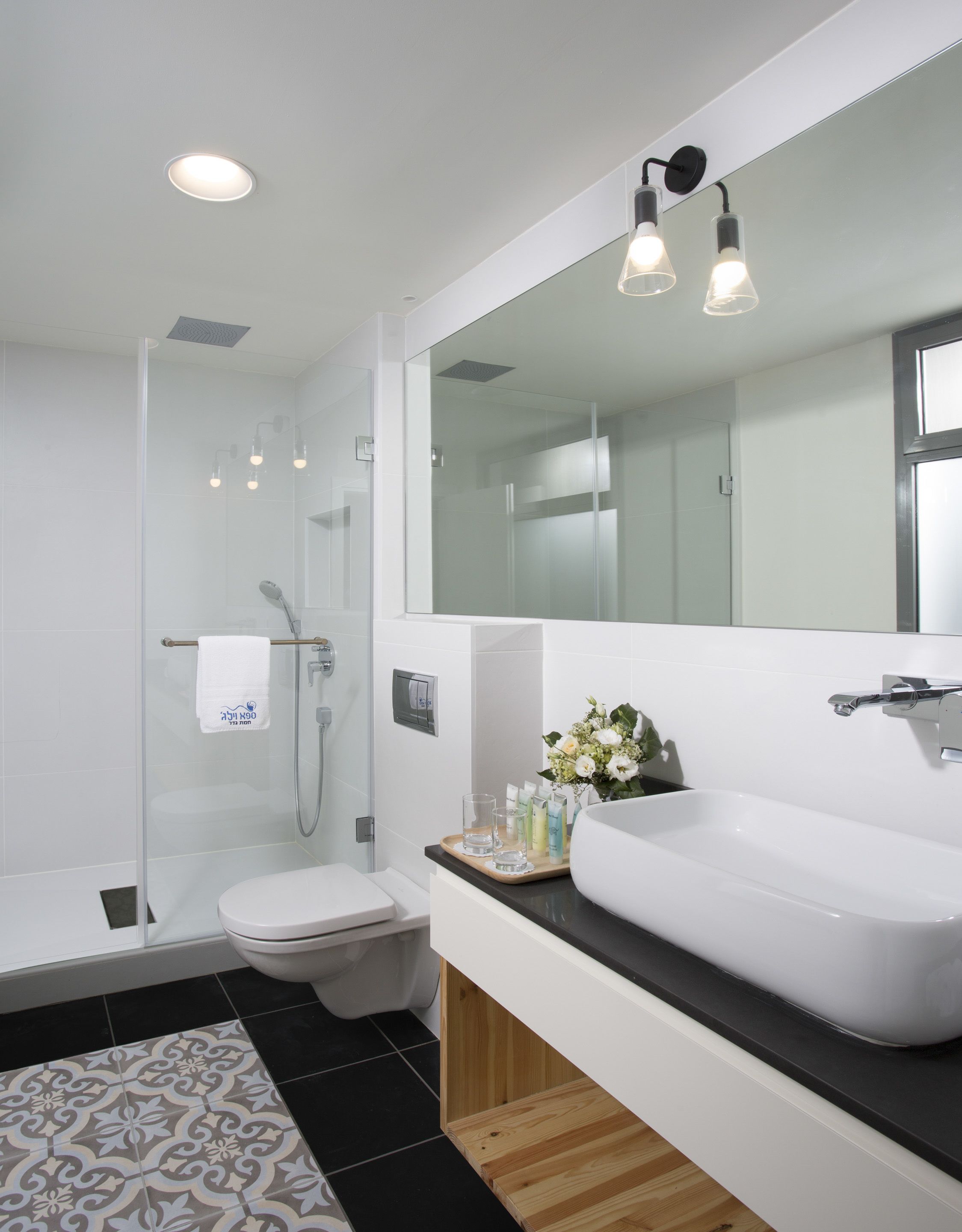 A modern bathroom with a white sink, a glass-enclosed shower, and a toilet.