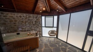A stone-walled bathroom with a wooden bathtub, a stone floor, and a wicker chair. - Spa Village Adults Only (Hamat Gader)