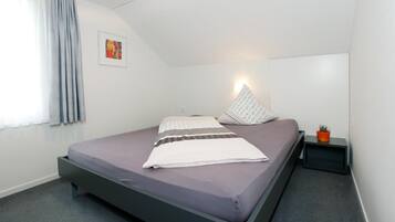 Ein modernes Schlafzimmer mit einem Bett, einer Nachttischlampe, einem kleinen Tisch mit einer Pflanze und einem Bild an der Wand.