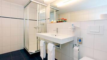 A modern bathroom with a glass shower enclosure, a white sink with a towel rack, and a toilet.