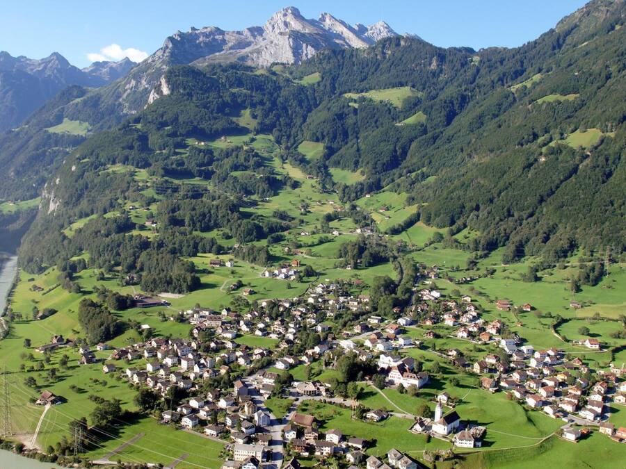 A village nestled in a valley with a river, surrounded by mountains.