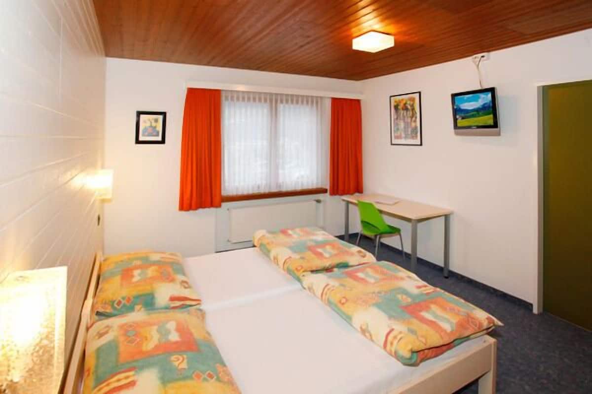 A room with two beds, a desk, a chair, and a window with curtains.