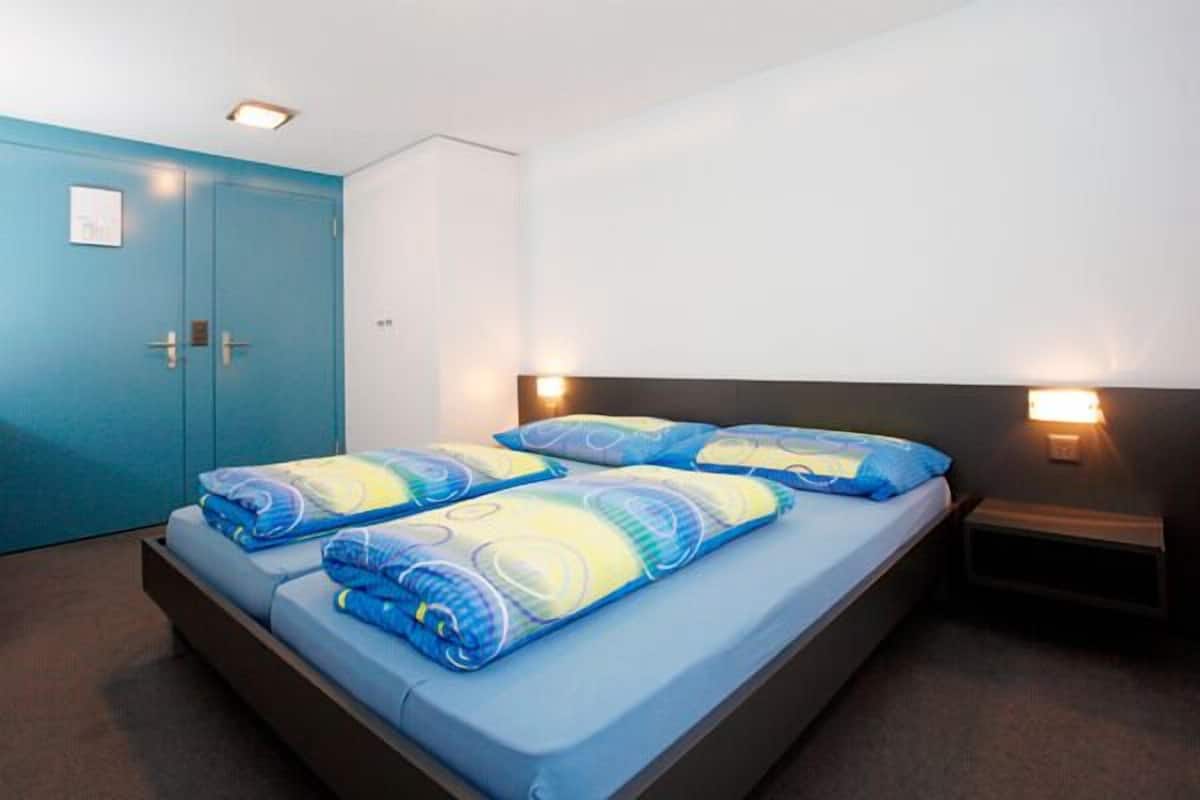 A hotel room with a bed, two bedside tables, and a blue door.