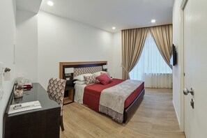 A hotel room with a bed, bedside table, chair, and a desk with a computer.