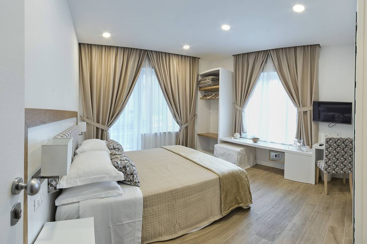 Una habitación de hotel moderna con una cama grande, mesitas de noche, un escritorio y un televisor.