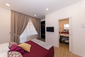 A hotel room with a bed, a TV, a bathroom with a sink and mirror, and a window with curtains.