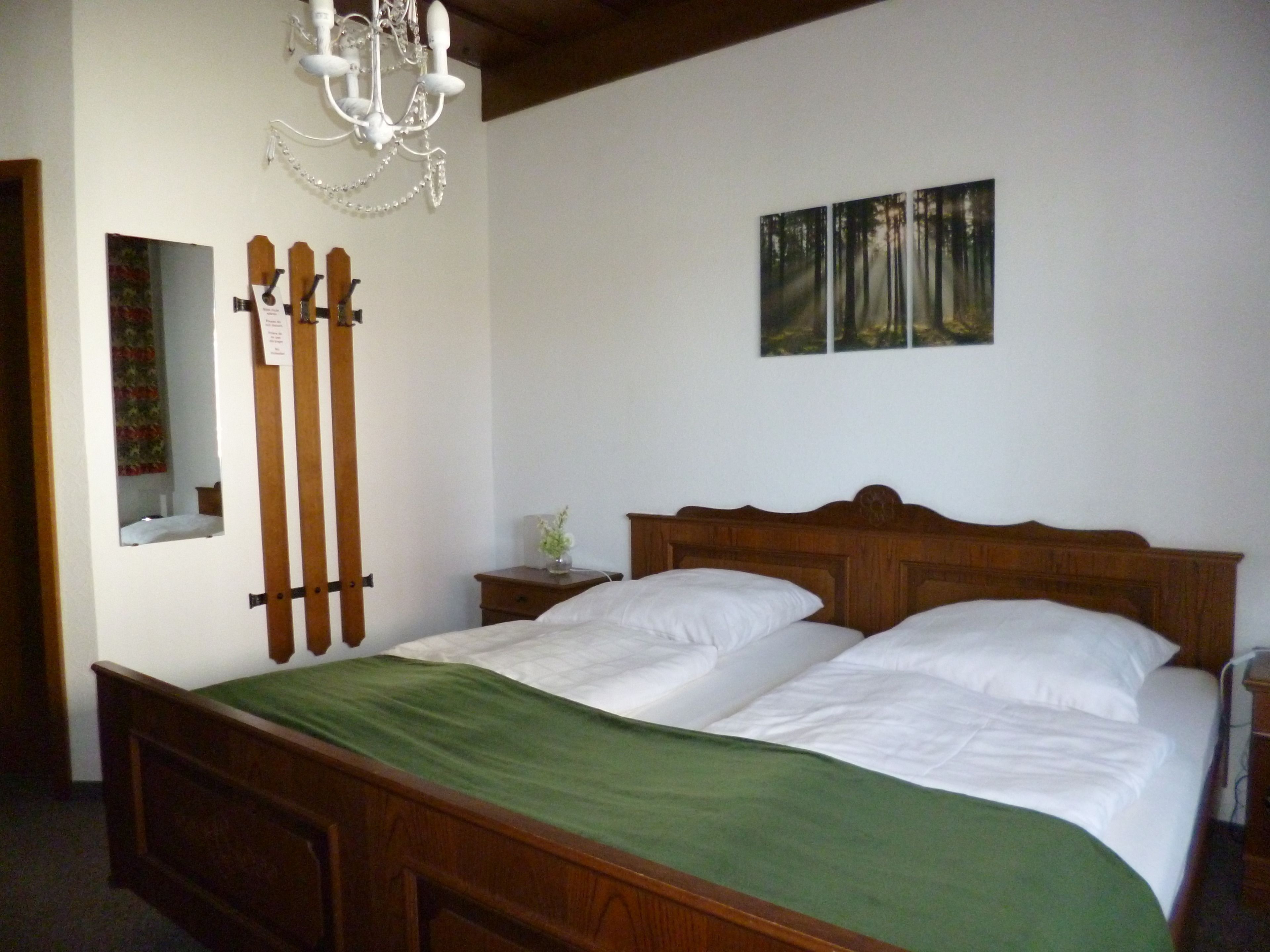 Un dormitorio con una cama de madera, un edredón verde, una lámpara de araña, un espejo y un cuadro de árboles en la pared.