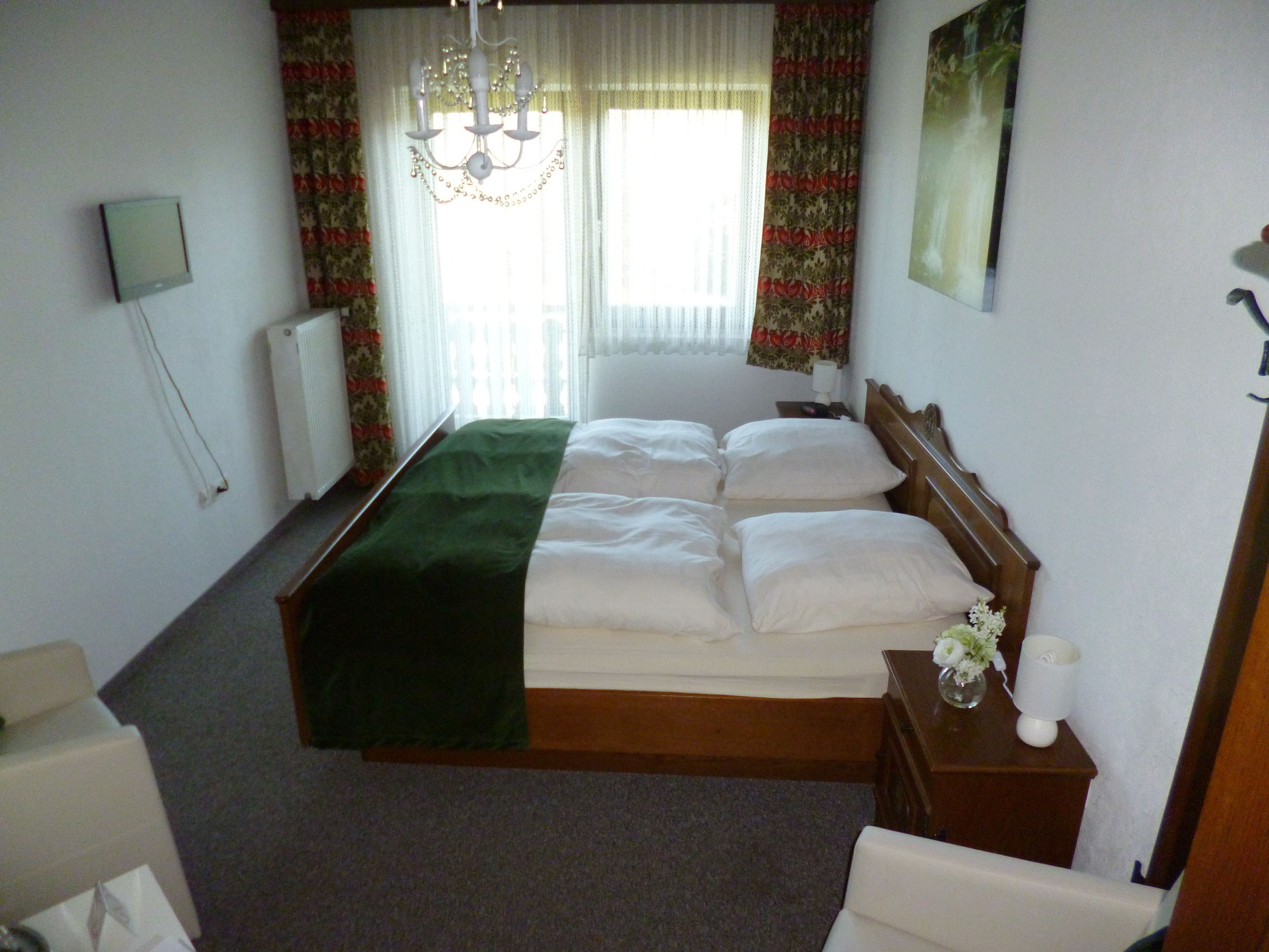 Une chambre d’hôtel avec un grand lit, une tête de lit en bois, une table de chevet ornée d’un vase de fleurs et un lustre.