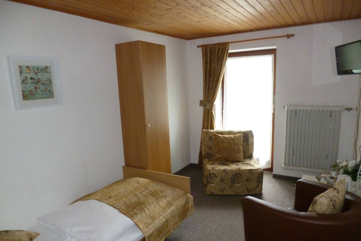 Ein Schlafzimmer mit einem Einzelbett, einem Holzschrank, einem Stuhl und einem Fernseher.