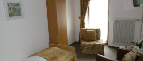 A bedroom with a single bed, a wooden wardrobe, a chair, and a television.