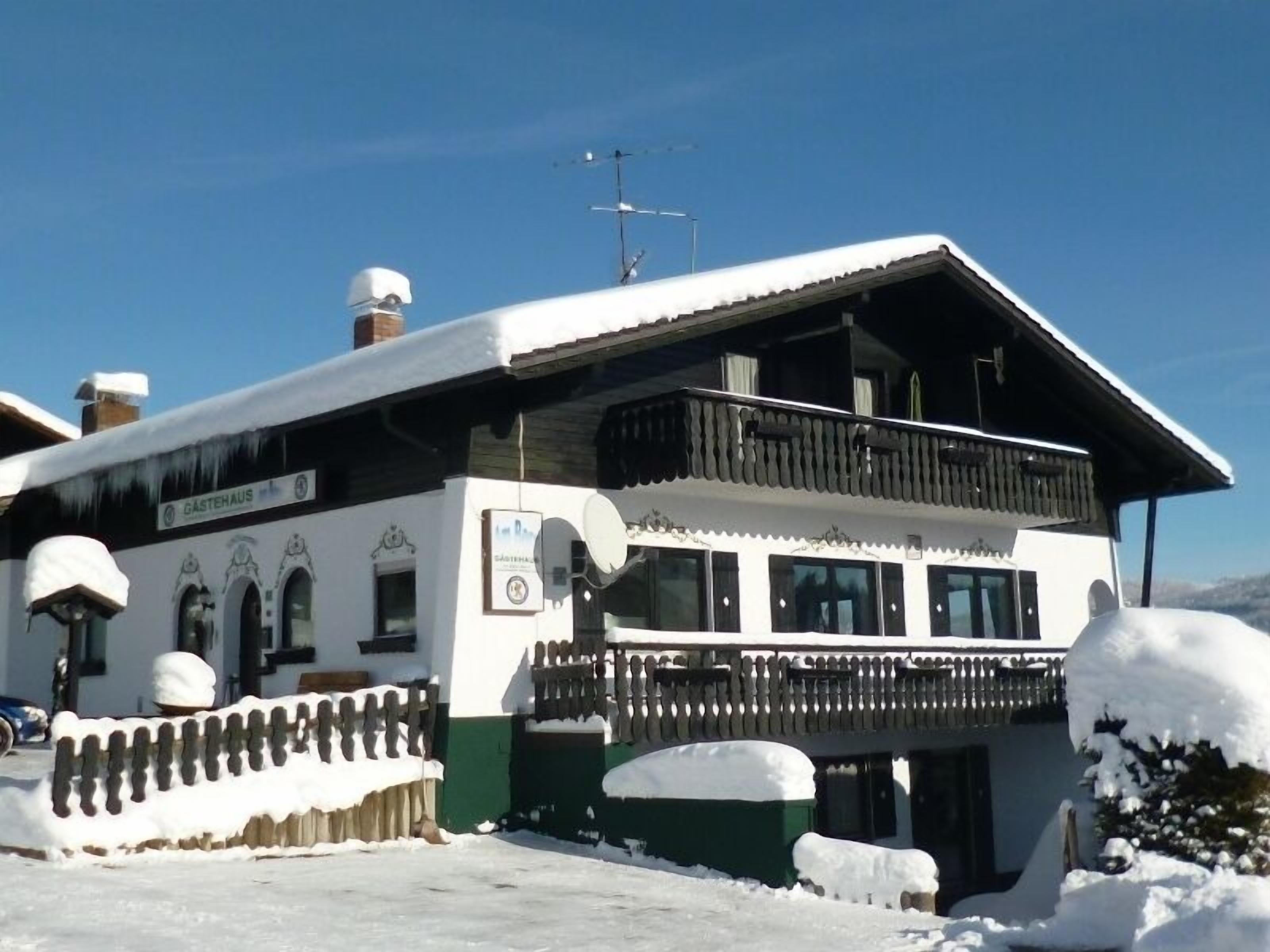 A traditional Alpine building with a sloped roof, a balcony, and a sign indicating it is a guesthouse.