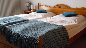 Una cama con cabecera de madera, ropa de cama blanca y una manta azul.