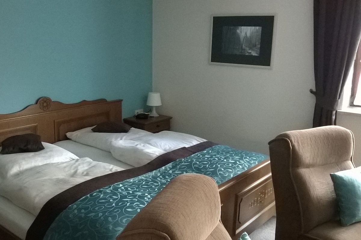 Ein Hotelzimmer mit Bett, Nachttisch, Stuhl und einem Gemälde an der Wand.