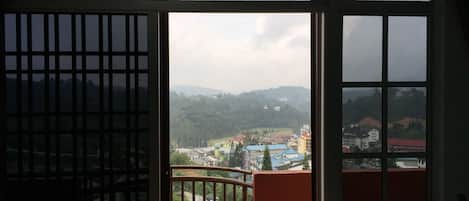 A view from a balcony with a metal railing, overlooking a town with buildings and hills in the background.