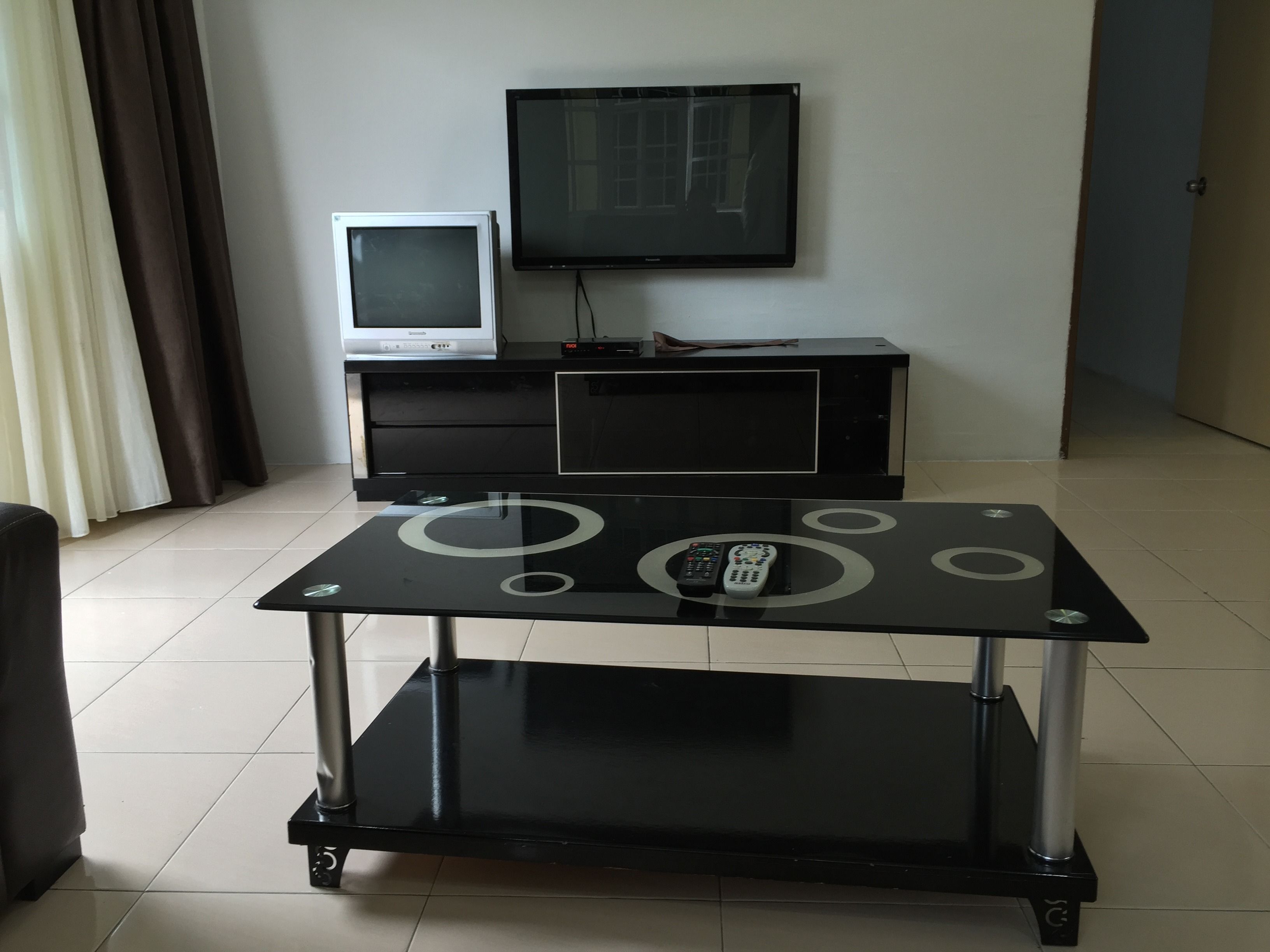 A modern living room with a glass-top coffee table, a flat-screen TV, and a vintage TV on a black cabinet.