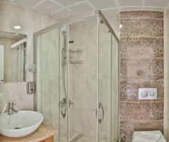 Un baño con cabina de ducha de vidrio, lavamanos y pared de azulejos con diseño geométrico.