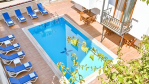 A swimming pool with lounge chairs and a table, surrounded by a wooden deck and a balcony with a railing.