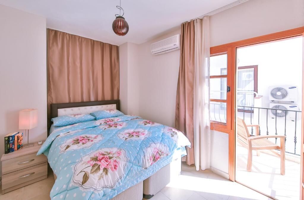A bedroom with a bed, a nightstand, a lamp, a window, and a balcony with a chair.