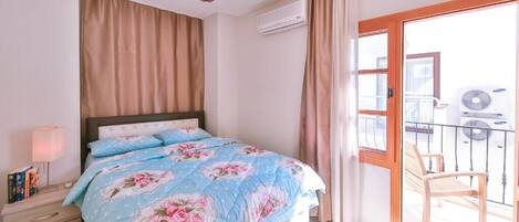 A bedroom with a bed, a nightstand, a lamp, a window, and a balcony with a chair.