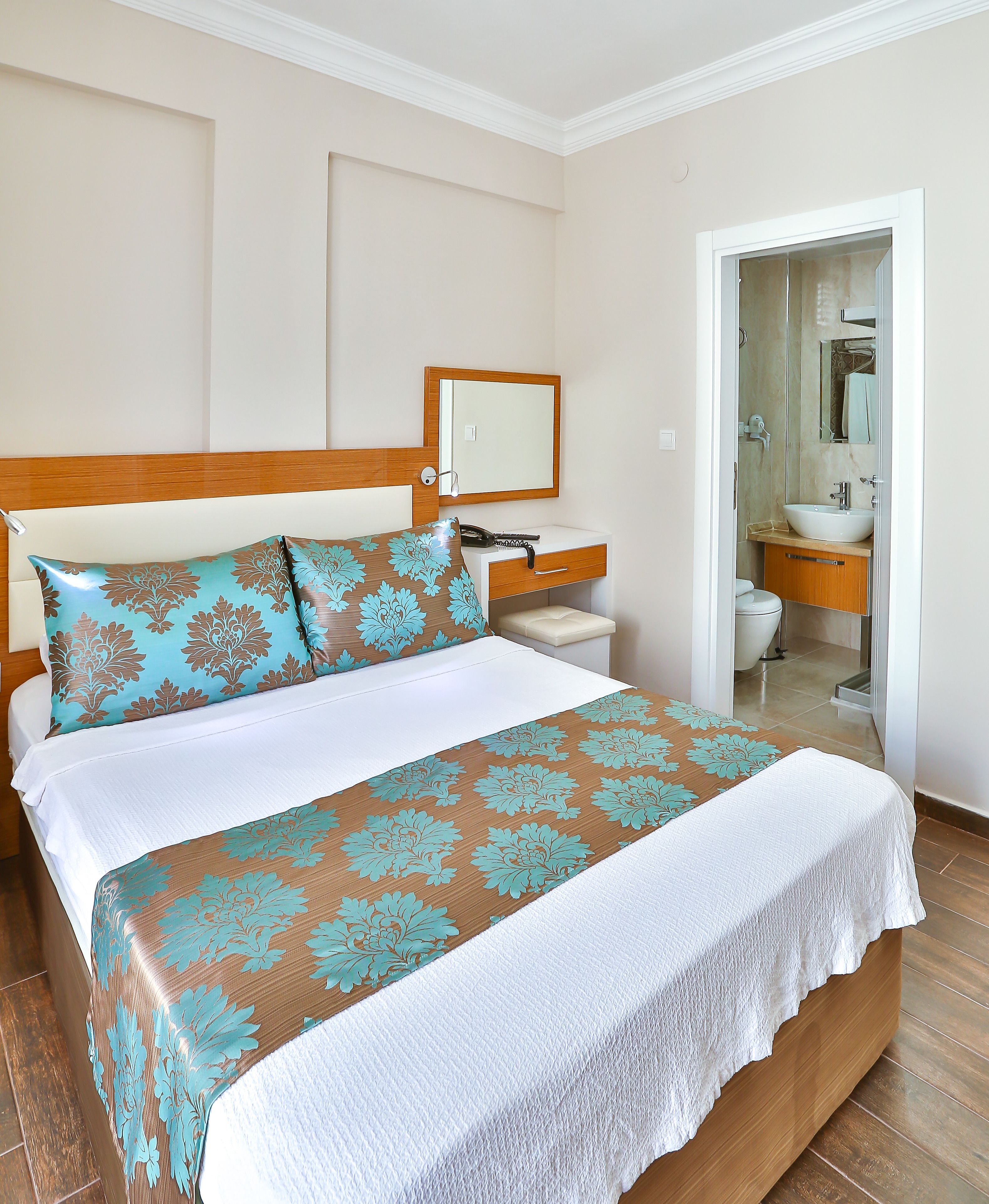 Ein Hotelzimmer mit einem Bett, einem Nachttisch, einem Spiegel und einem durchgegangenen Tür angedeuteten Badezimmer.