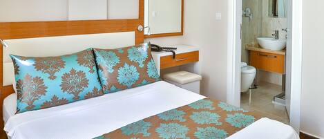 A hotel room with a bed, a bedside table, a mirror, and a bathroom visible through an open door.