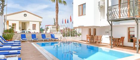 Un área de piscina con sillones de descanso y un edificio con balcones.