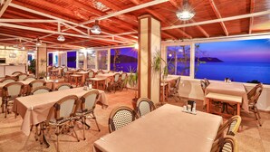 A restaurant with multiple tables and chairs, a wooden ceiling, and large windows overlooking a scenic view.