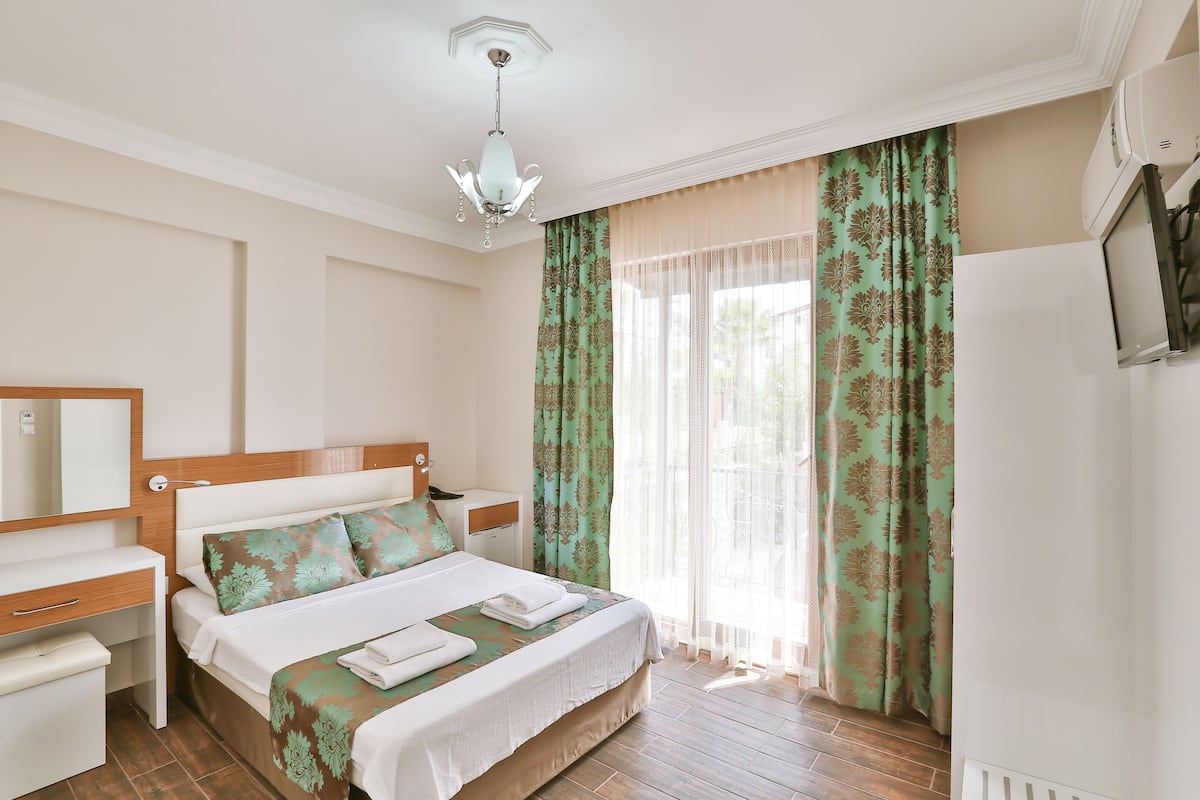 Une chambre d’hôtel avec deux lits, un bureau, un miroir et une fenêtre avec des rideaux.