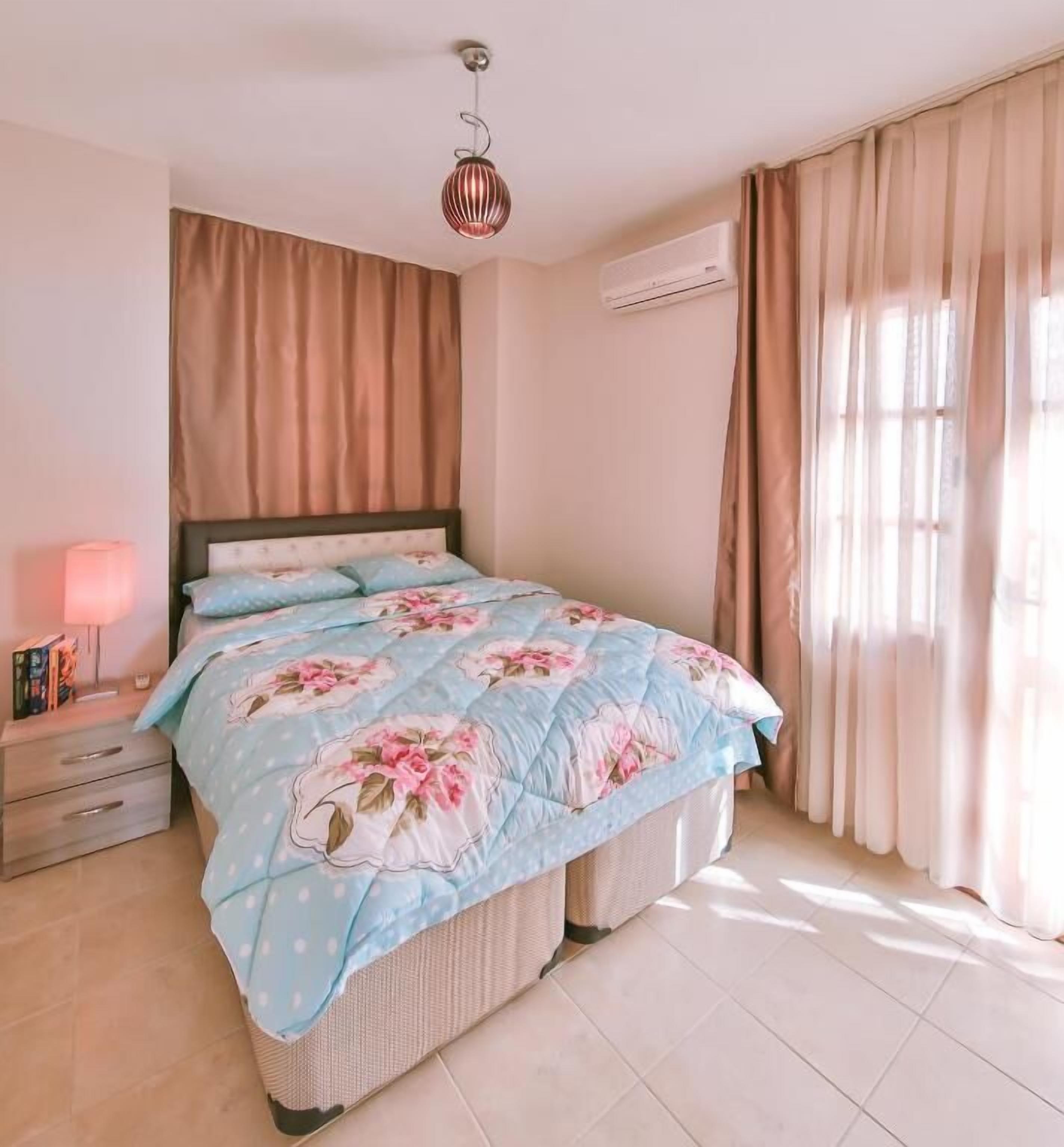 Un dormitorio con cama, mesita de noche, lámpara y cortinas.