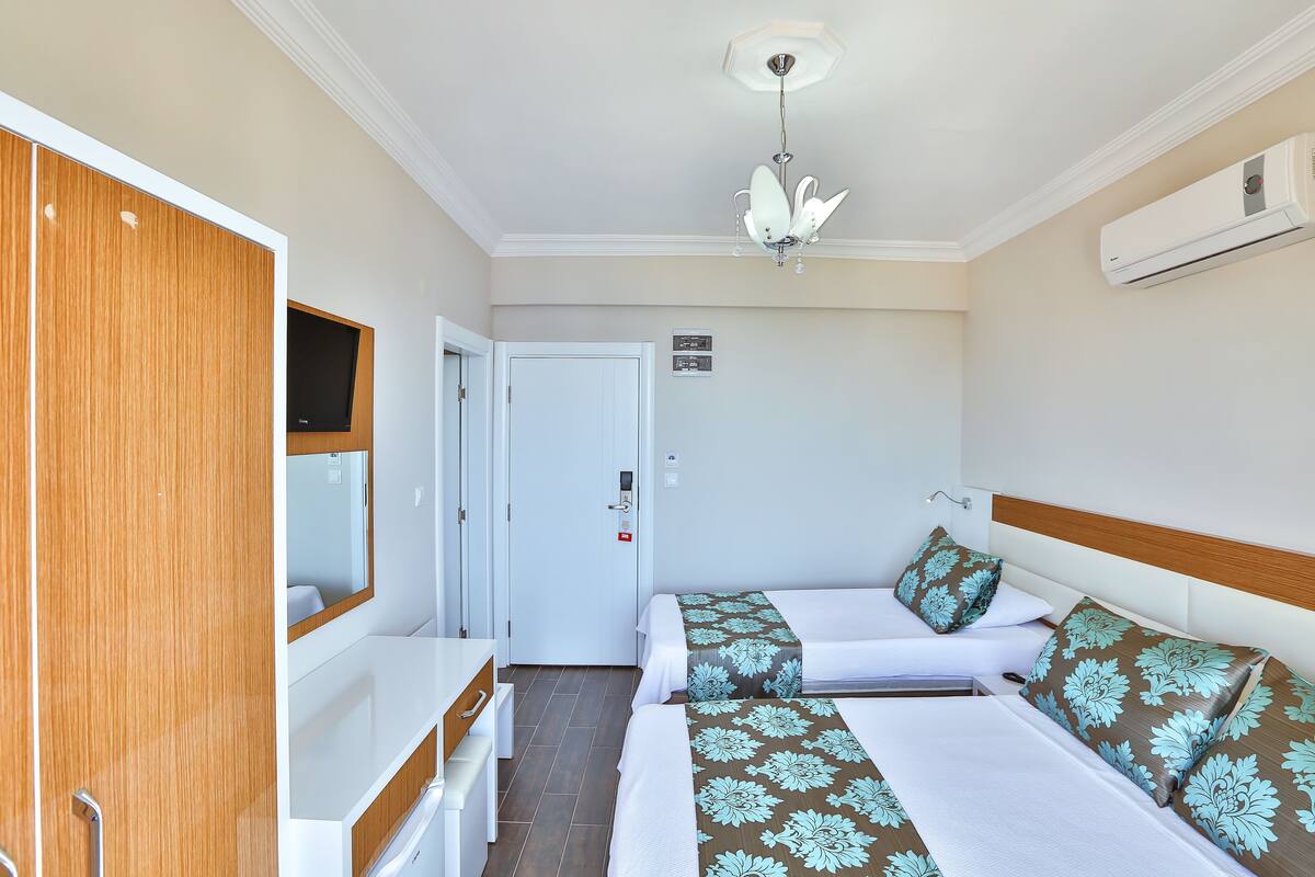 Une chambre d’hôtel avec deux lits, un bureau, un miroir, un ventilateur de plafond et un appareil de climatisation.