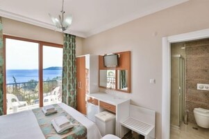 Habitación de hotel con balcón, cama, escritorio, televisor y baño.