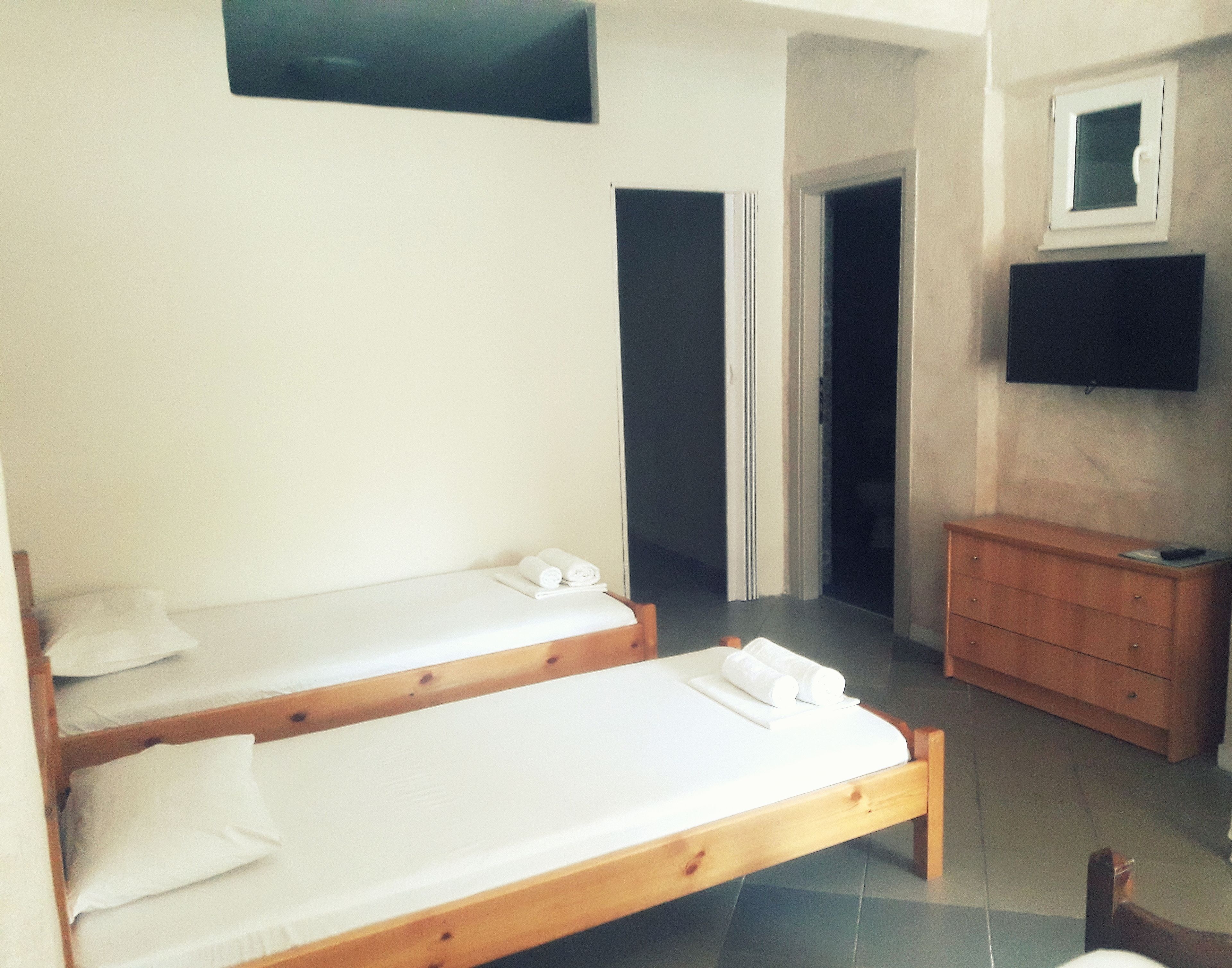 A room with two wooden beds, a wooden dresser, and a television mounted on the wall.