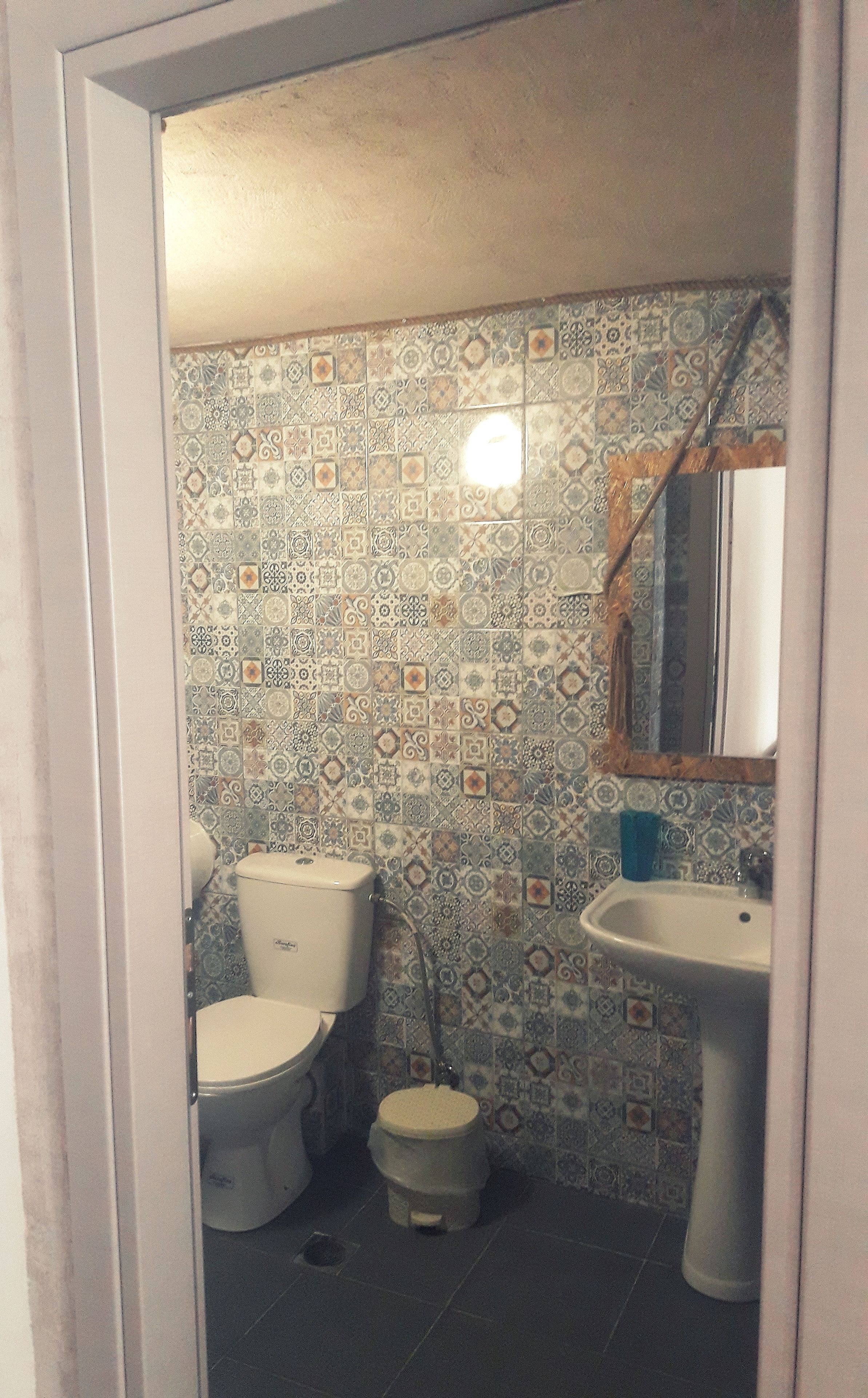 A bathroom with a toilet, bidet, and sink, tiled with a patterned design.