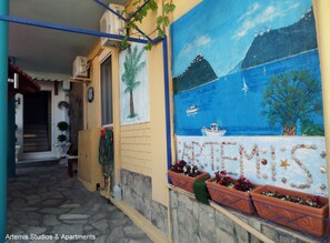 Un mural con temática costera que muestra un barco, un faro, plantas en macetas y una escalera que lleva a una puerta.