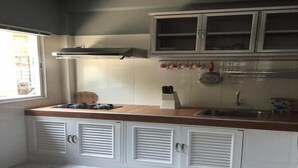 A kitchen with white cabinets, a wooden countertop, a gas stove, a sink, and a window with blinds. - Nicha Homestay Huahin (Hua Hin)