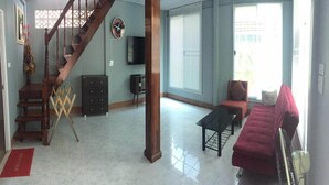 A spacious living room with a wooden staircase, a red sofa, a black coffee table, and a large window with blinds. - Nicha Homestay Huahin (Hua Hin)