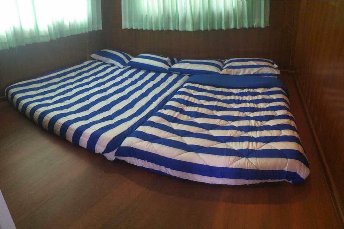 A room with a large bed covered in a striped blanket, wooden flooring, and a window with sheer curtains.