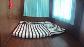 A room with a wooden floor, a striped sofa, and a window with light blue curtains. - Nicha Homestay Huahin (Hua Hin)