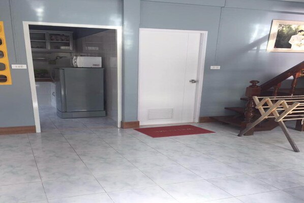 A room with a kitchen area, a white door, and a staircase with a wooden handrail.
