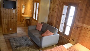 A cozy room with a grey sofa, a small table, and a bed. - Studios du Valsorey (Bourg-Saint-Pierre)