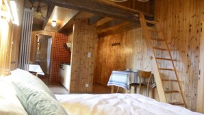 A wooden cabin interior with a bed, a table with chairs, a ladder, and a bathroom visible through a door. - Studios du Valsorey (Bourg-Saint-Pierre)