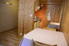 A compact room with a wooden interior, a kitchenette, a table with a white tablecloth, and a chair.