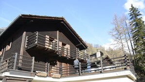 A wooden chalet with a balcony and a white lower section. - Studios du Valsorey (Bourg-Saint-Pierre)