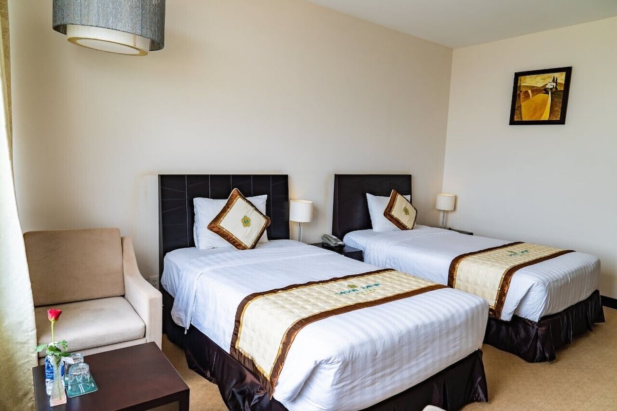Une chambre d’hôtel avec deux lits, un canapé, une petite table avec un vase et une bouteille, et un tableau au mur.