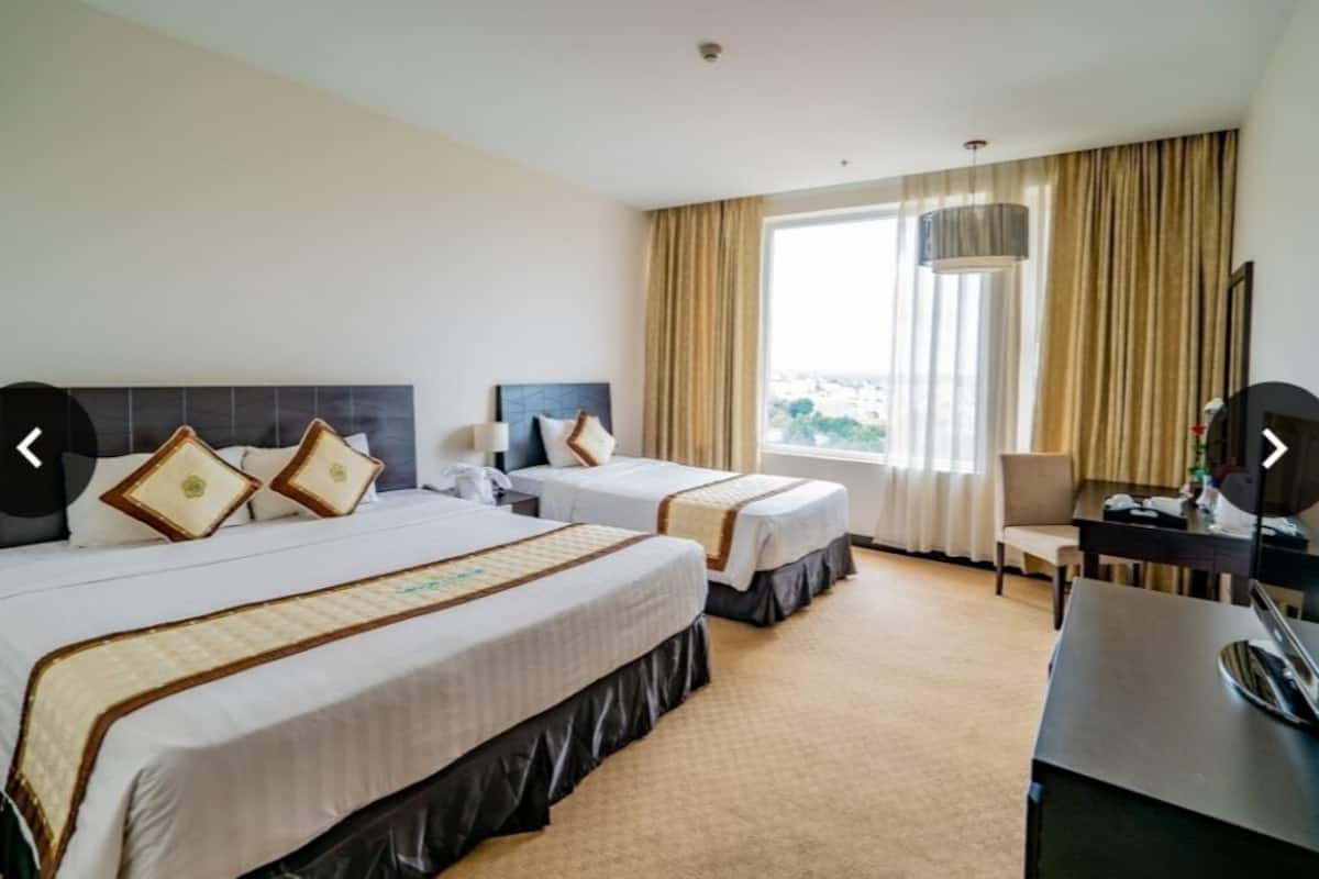 Une chambre d’hôtel avec deux lits, un bureau, une chaise et une grande fenêtre avec des rideaux.